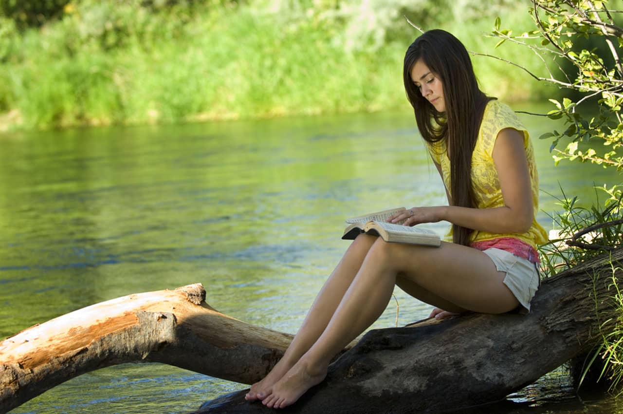 Eine Frau sitzt auf einem Baum am See und liest ein Buch